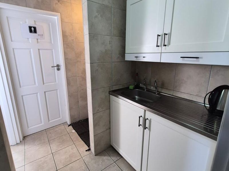 A functional scullery or kitchenette area featuring white built-in cabinetry, a stainless steel sink, and neutral tiled finishes.