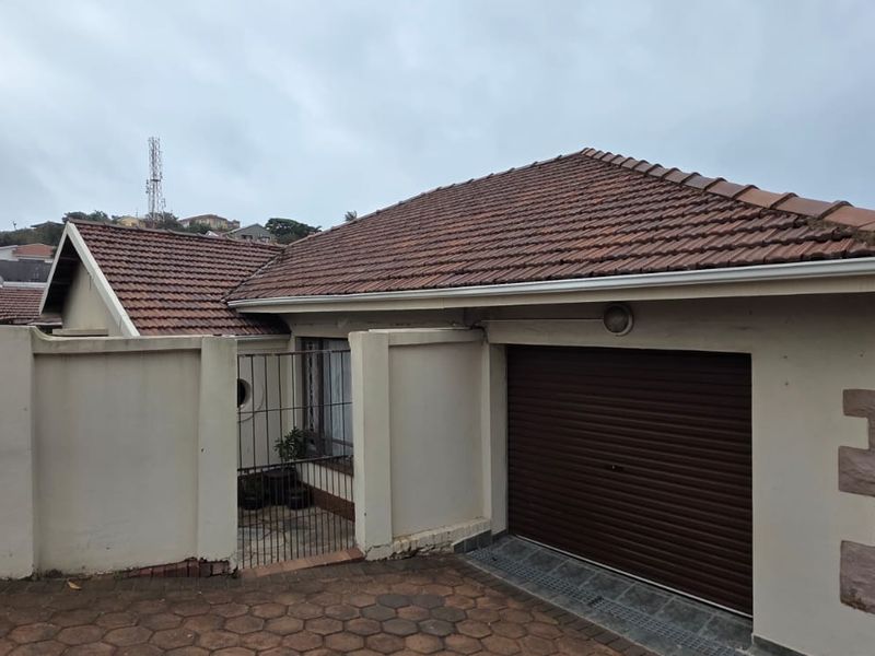 Front exterior view of the property featuring a tiled roof, roller garage door, paved driveway, and secure boundary walling.