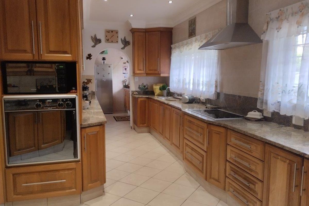 A functional kitchen featuring warm-toned wooden cabinetry, granite countertops, built-in oven, electric cooktop, and tiled flooring with an adjacent scullery area.