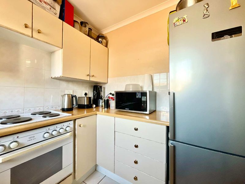 A compact kitchen featuring built-in cabinetry, laminate countertops, a tiled backsplash, and a freestanding electric stove and oven.
