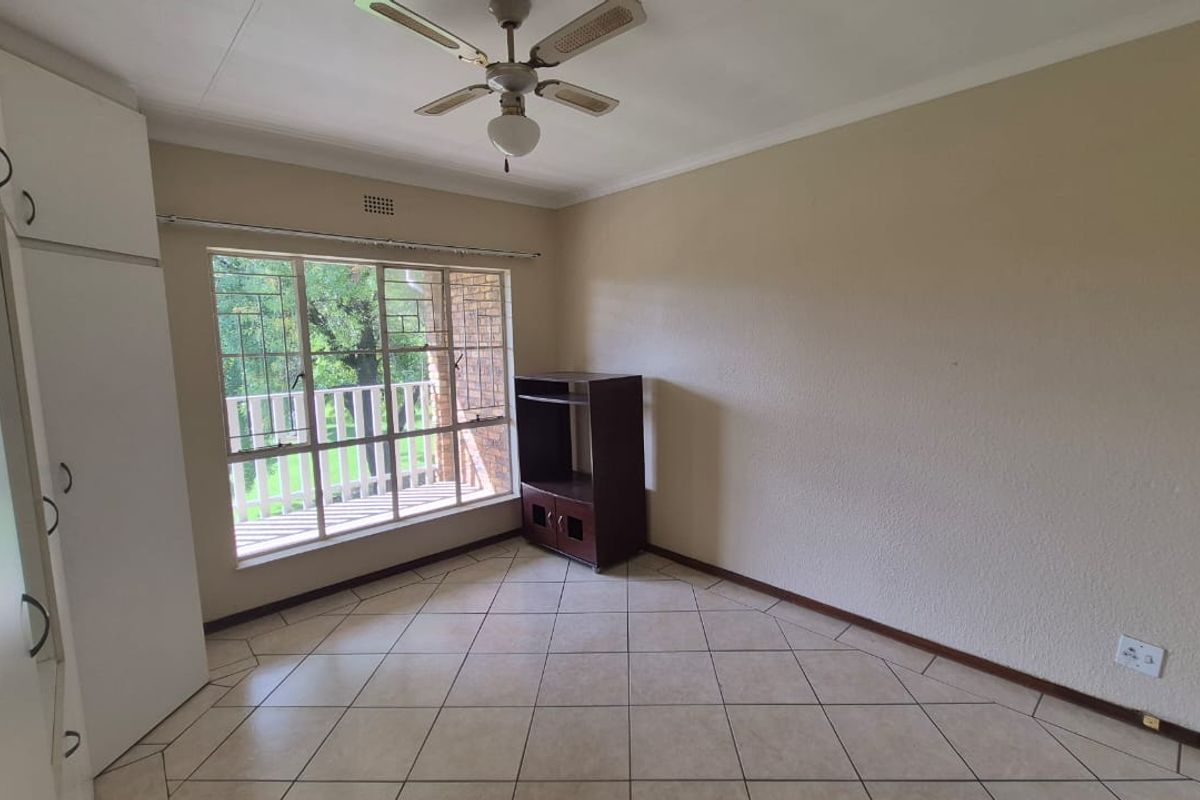 A bedroom featuring built-in cupboards, tiled flooring, a ceiling fan, and large windows providing natural light.