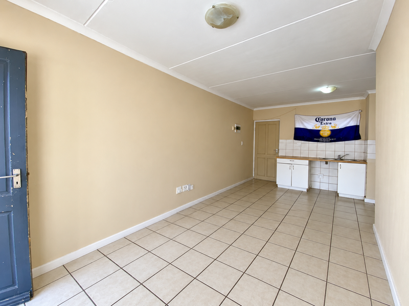 An open-plan living and kitchen area featuring tiled flooring, neutral walls, and basic kitchen cabinetry with a sink.