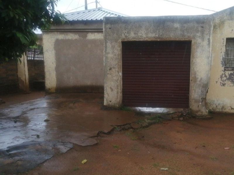 A detached garage featuring a roller shutter door and a weathered concrete driveway with visible surface cracking and exterior wall deterioration.