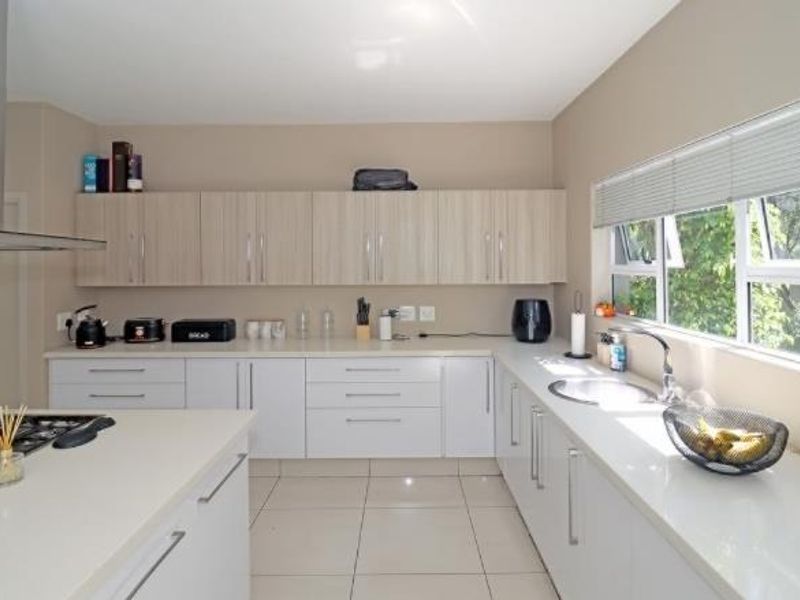 Modern kitchen featuring sleek white and wood-tone cabinetry, quartz countertops, a gas hob with stainless steel extractor, and large windows for natural light.