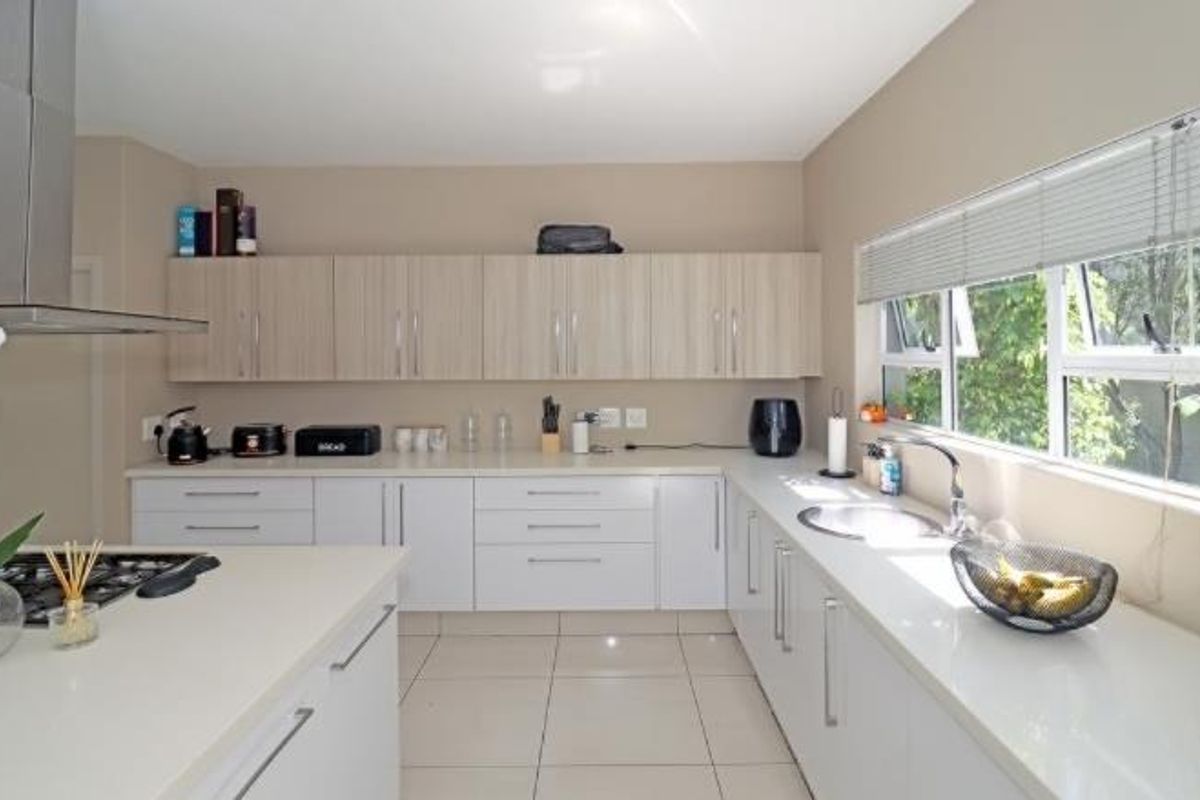 Modern kitchen featuring sleek white and wood-tone cabinetry, quartz countertops, a gas hob with stainless steel extractor, and large windows for natural light.
