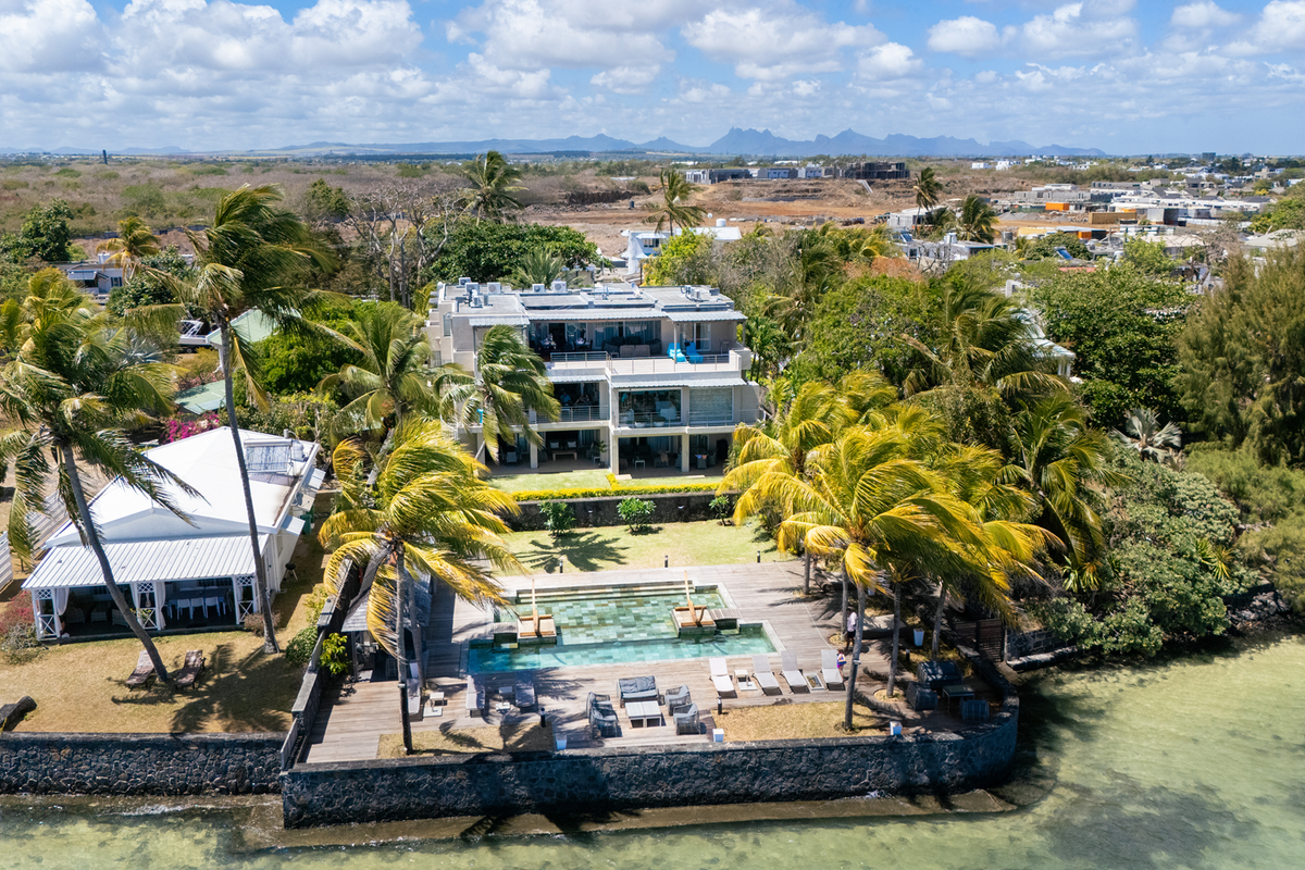 Aerial view of a waterfront apartment complex featuring a swimming pool, wooden decking, and landscaped gardens overlooking the ocean.