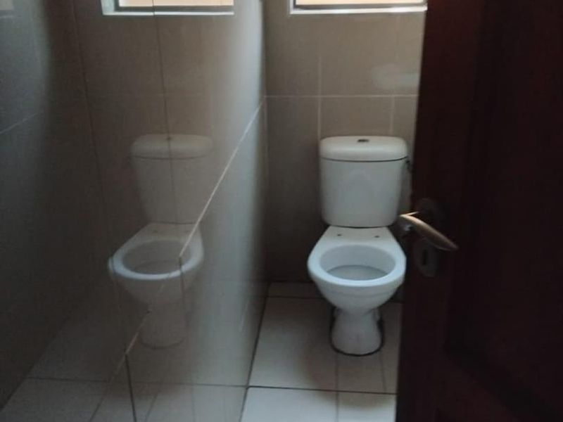 A clean, functional guest bathroom featuring tiled walls, tiled flooring, and a private toilet with a frosted glass window for natural light.