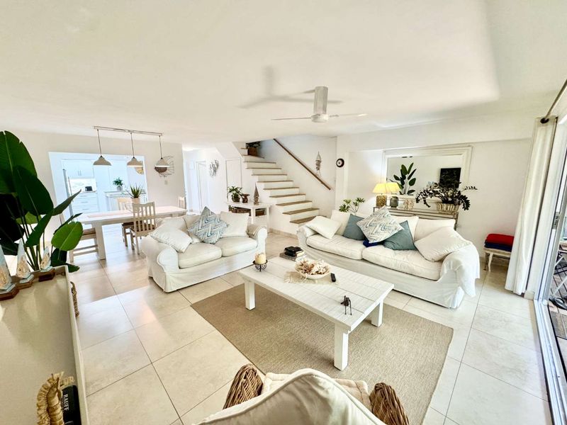 Spacious open-plan living and dining area featuring neutral tiled flooring, a central staircase, and large sliding glass doors providing ample natural light.