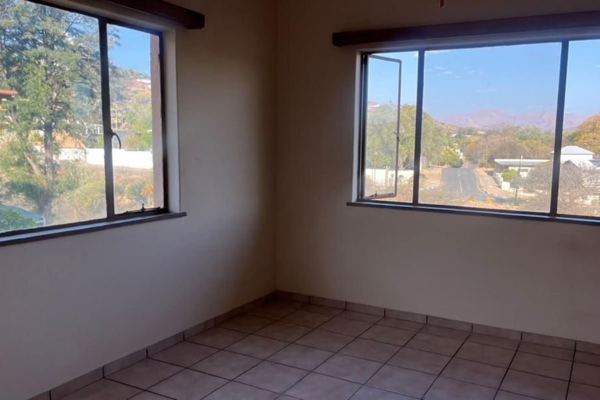 An empty bedroom featuring tiled flooring and large windows that provide ample natural light and scenic views of the surrounding neighborhood.