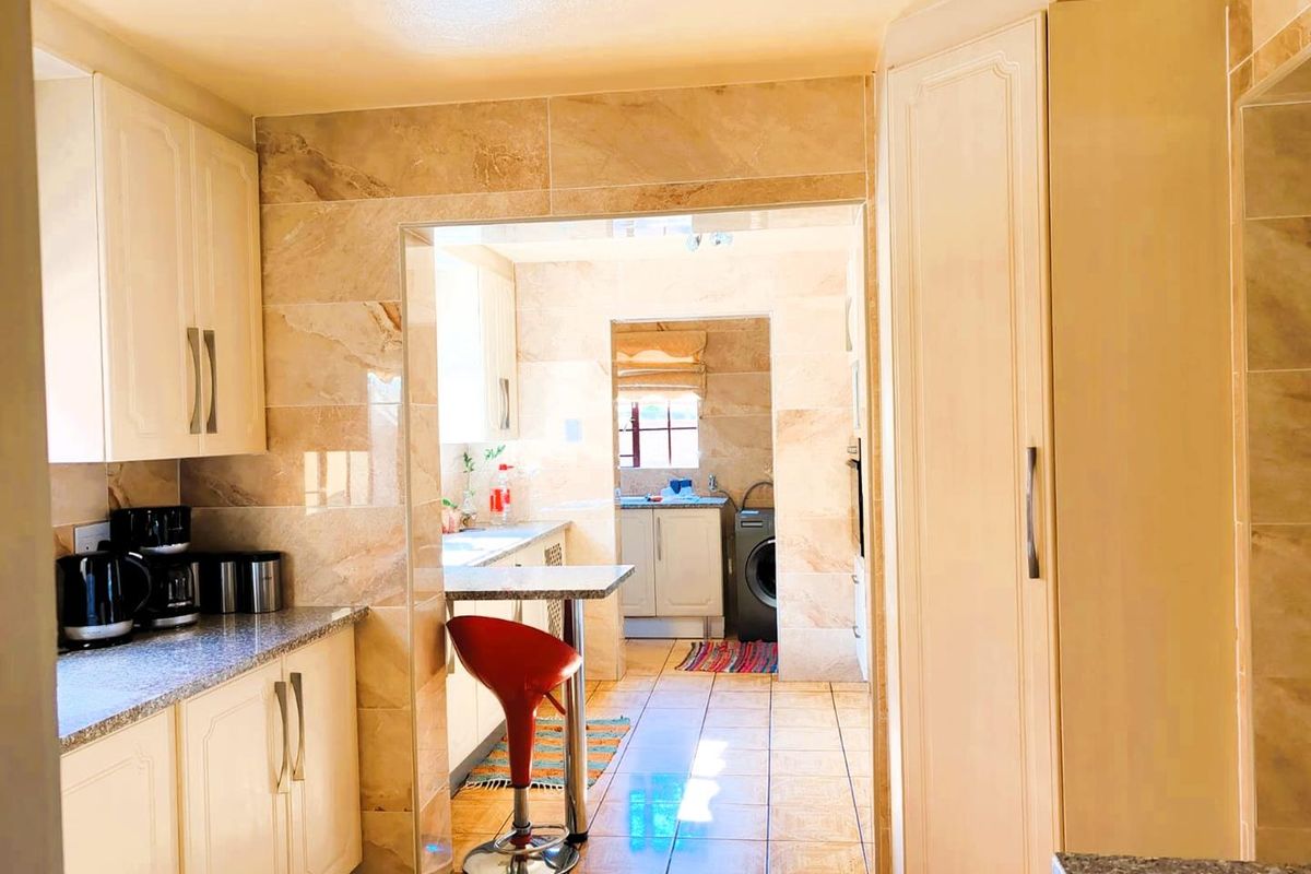 A functional kitchen featuring tiled walls and flooring, ample cabinetry, and a connected scullery area with laundry facilities.