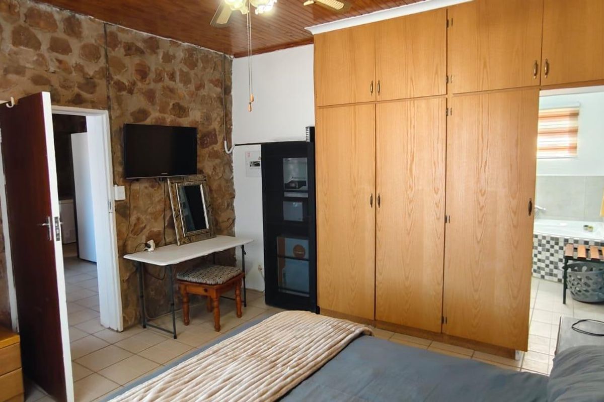 Bedroom featuring a stone accent wall, timber ceiling, and extensive built-in wooden cupboards, with an adjoining en-suite bathroom.