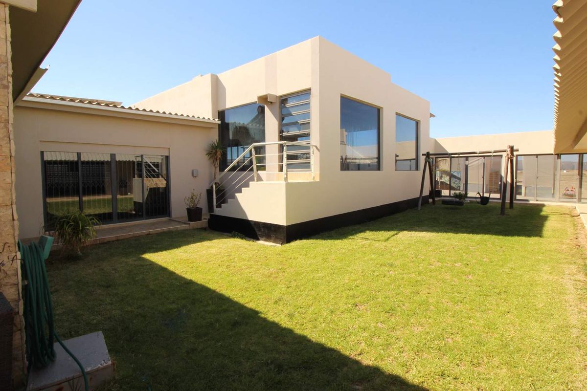 Rear view of the property featuring a modern architectural design, large glass windows, an external staircase, and a well-maintained lawn area.