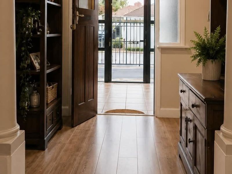 Welcoming entrance hall featuring timber flooring, decorative columns, and a solid timber front door leading to a secure gated porch area.