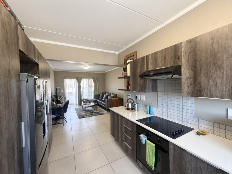 Modern open-plan kitchen and living area featuring contemporary cabinetry, integrated appliances, tiled flooring, and direct access to a balcony through sliding glass doors.