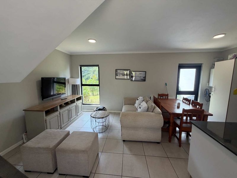 An open-plan living and dining area featuring neutral tiled flooring, recessed lighting, and large windows that provide natural light and garden views.