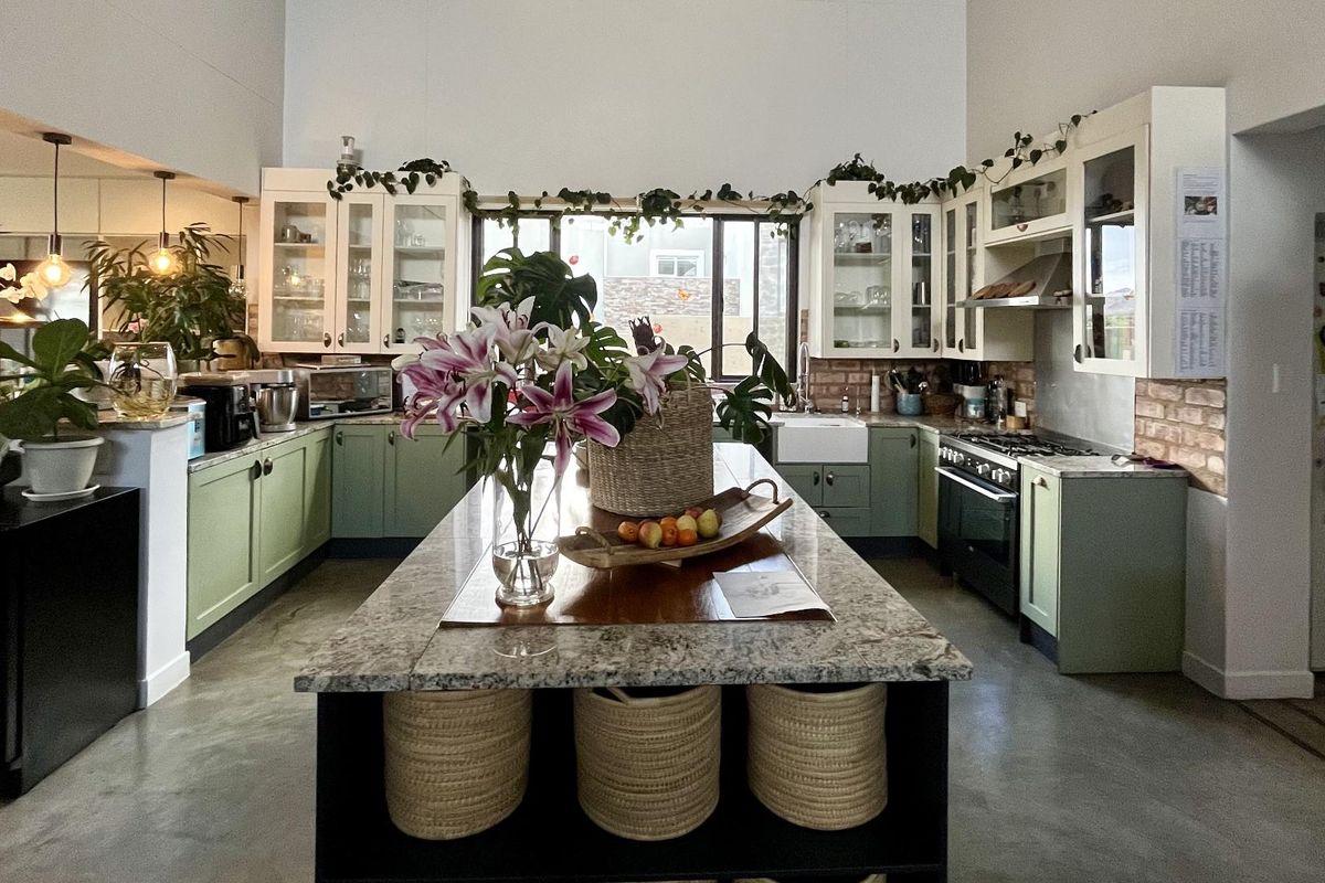 Spacious kitchen featuring a large central island, granite countertops, farmhouse sink, gas range, and stylish green cabinetry with exposed brick accents.