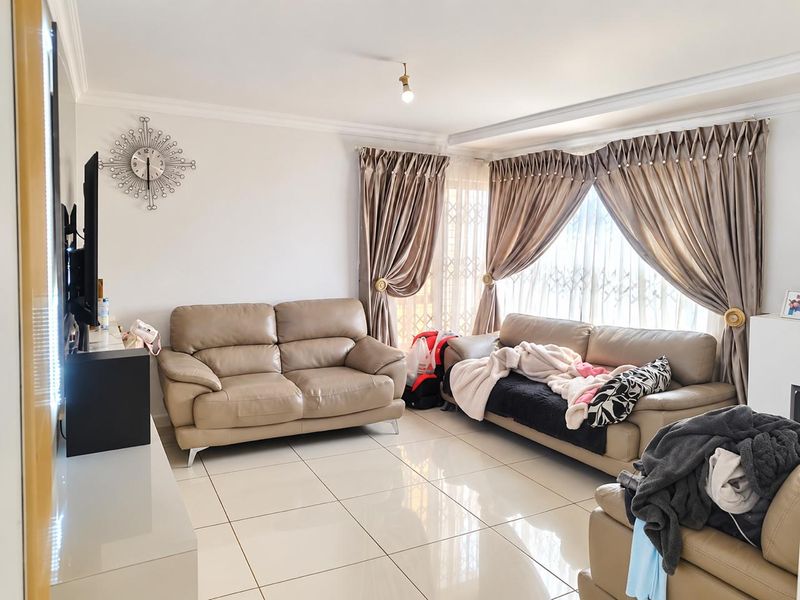 A bright living room featuring polished floor tiles, coved ceilings, and large windows fitted with decorative curtains and security gates.