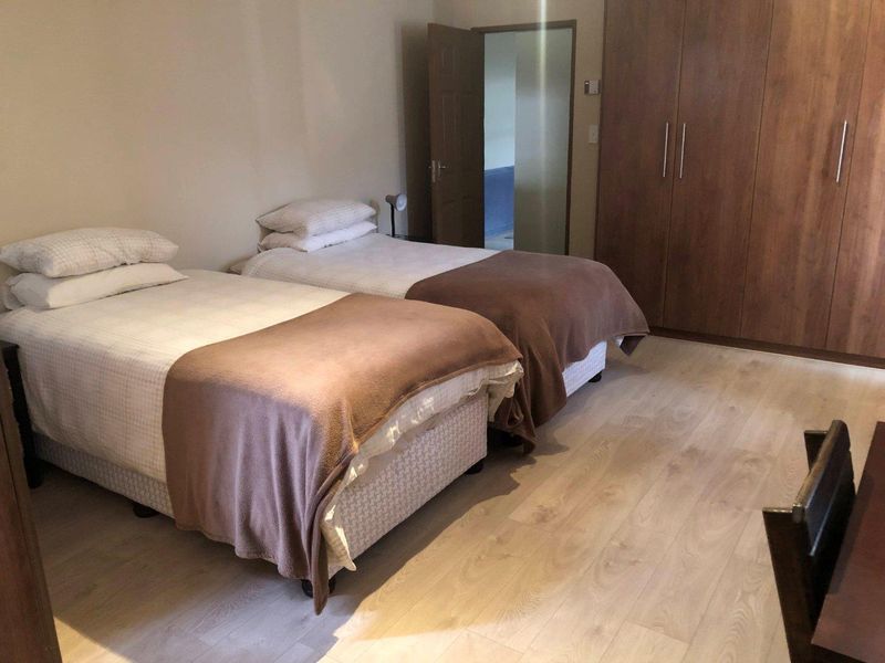 A functional bedroom featuring light-toned laminate flooring and a large built-in wooden wardrobe providing ample storage space.
