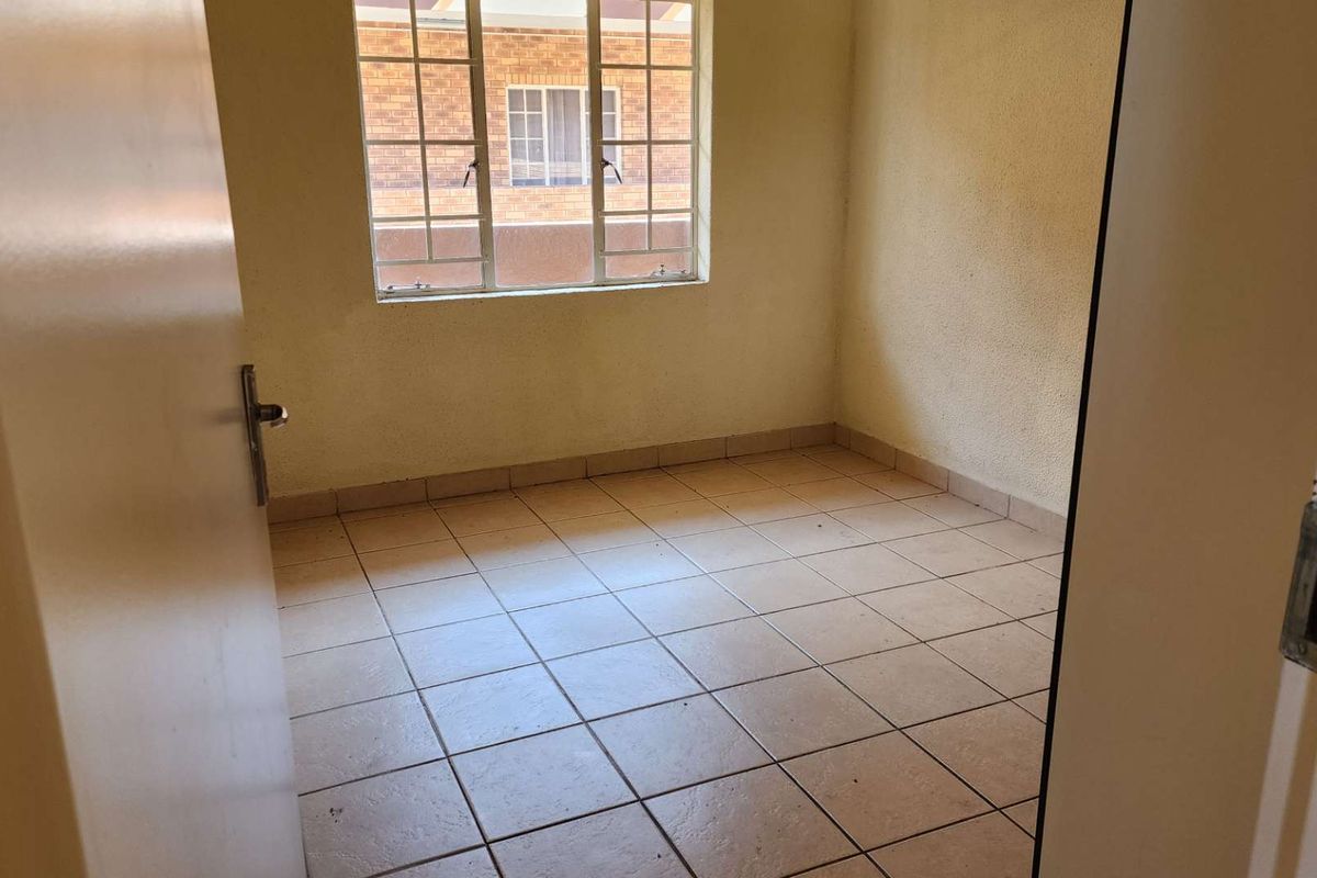 An empty bedroom featuring tiled flooring and a window with security bars, offering a blank canvas for renovation.