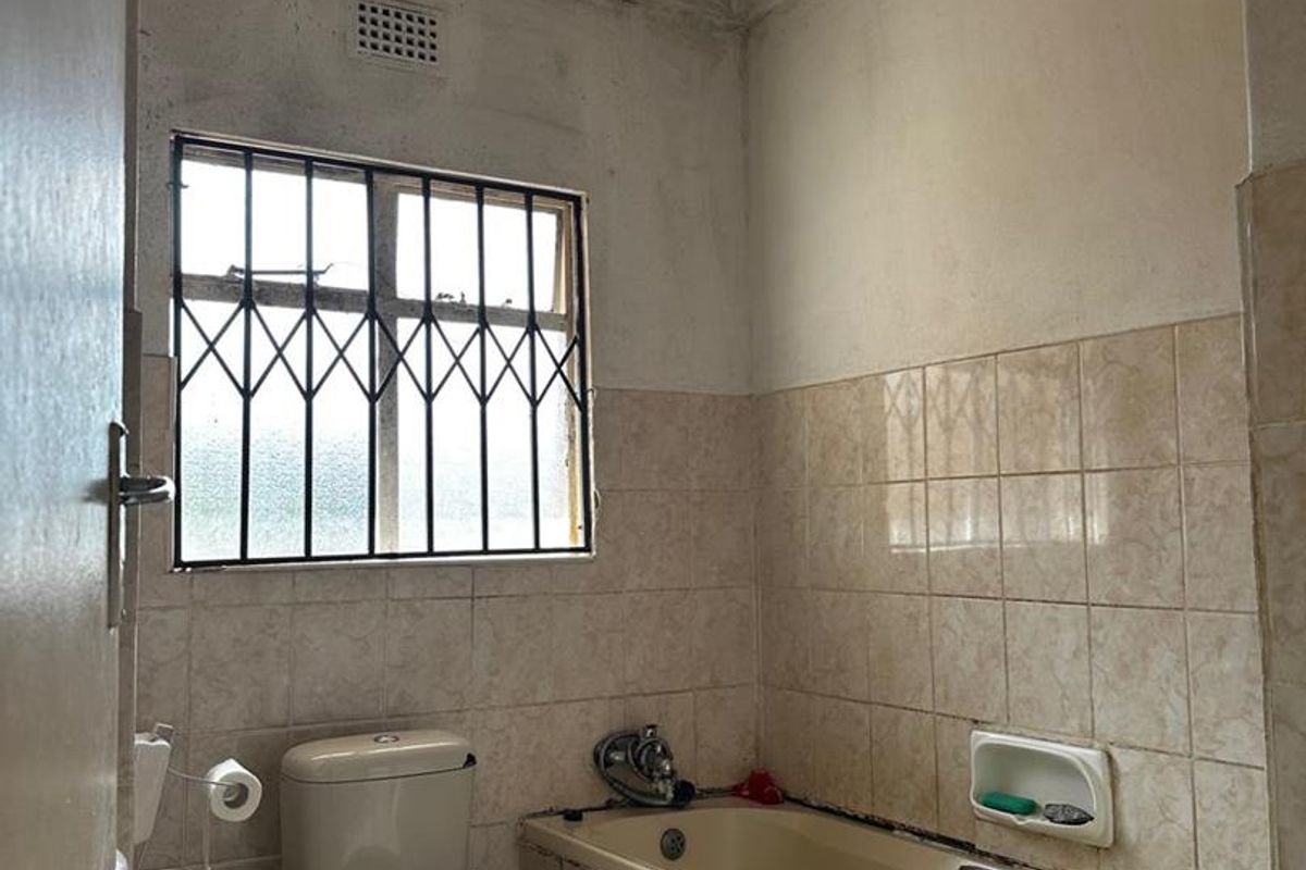 A dated bathroom featuring a built-in bathtub, toilet, and tiled walls. The space requires significant renovation and cosmetic updates to improve its condition.