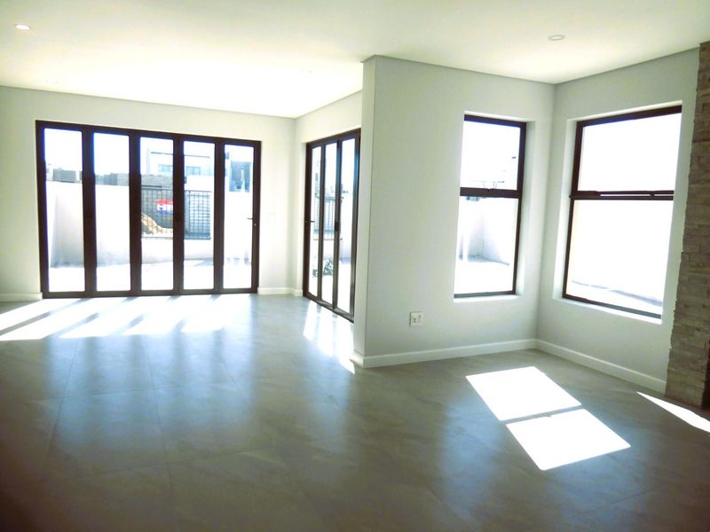 A bright, modern, and empty living area featuring large stacking doors, tiled floors, recessed lighting, and a stone-clad feature wall.