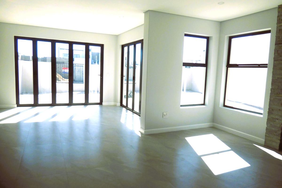 A bright, modern, and empty living area featuring large stacking doors, tiled floors, recessed lighting, and a stone-clad feature wall.