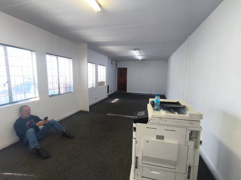 A vacant industrial office space featuring carpet flooring, security-barred windows, and fluorescent lighting, suitable for a variety of commercial or administrative uses.