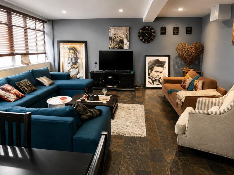A spacious living room featuring dark tiled flooring, recessed ceiling lighting, and large windows with venetian blinds.