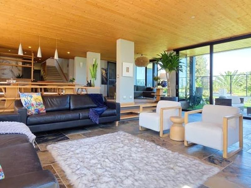 Spacious open-plan living area featuring natural timber ceilings, stone flooring, and expansive floor-to-ceiling glass doors providing seamless indoor-outdoor flow.
