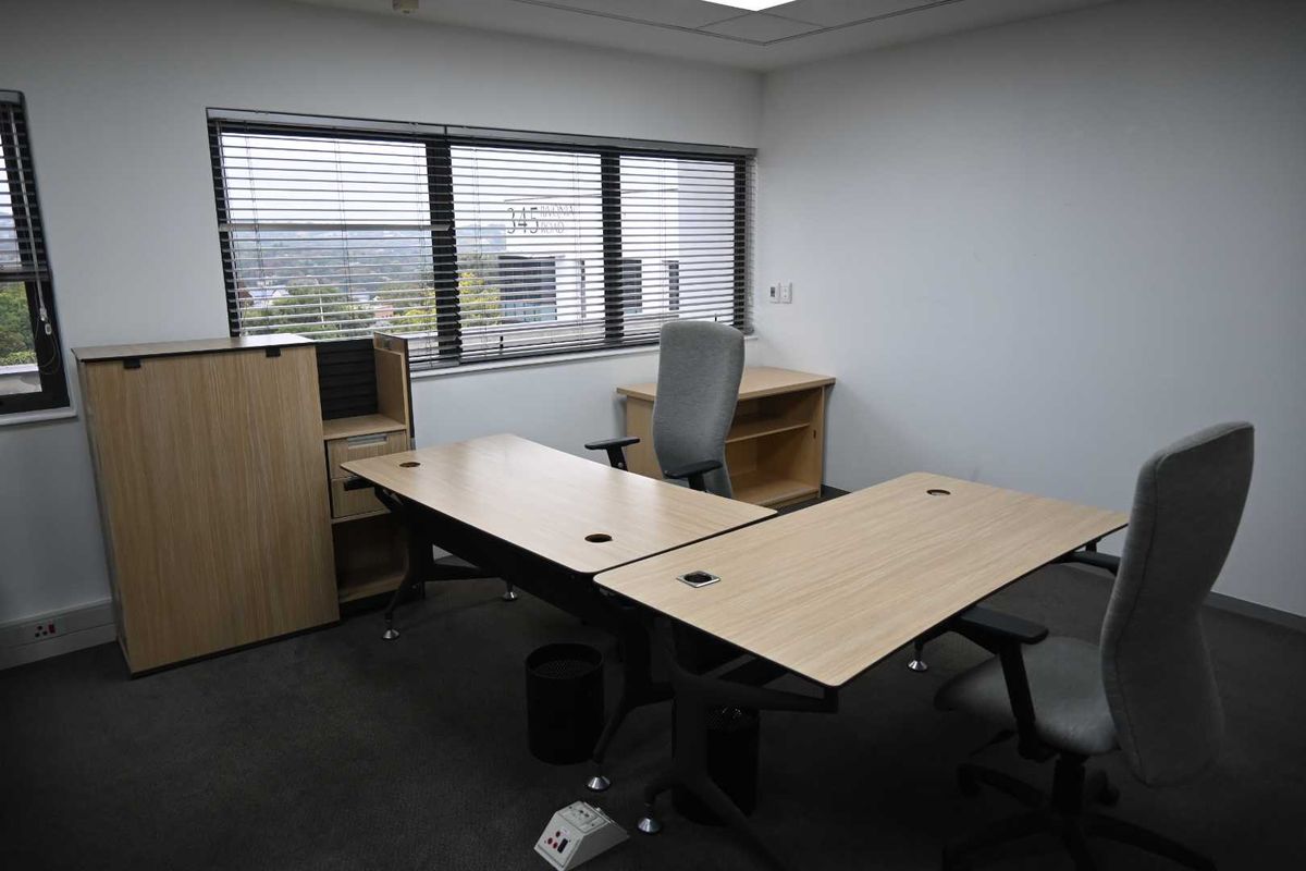 A functional office space featuring carpeted flooring, recessed ceiling lighting, and large windows with venetian blinds providing natural light.