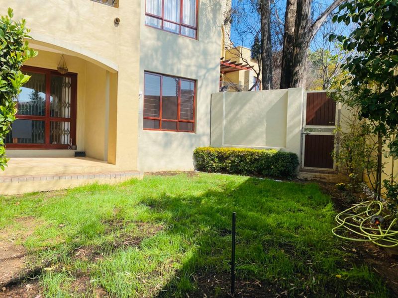 Rear view of the apartment featuring a covered patio, sliding glass doors with security gates, and a private garden area with a boundary wall.