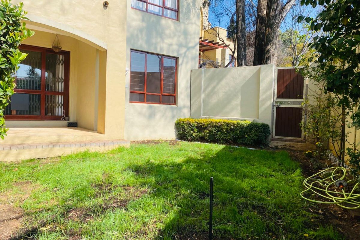 Rear view of the apartment featuring a covered patio, sliding glass doors with security gates, and a private garden area with a boundary wall.