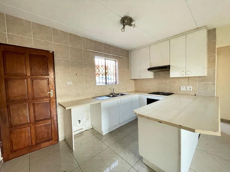 A functional kitchen featuring white built-in cabinetry, tiled splashbacks, a double sink, and a built-in hob with an extractor fan.
