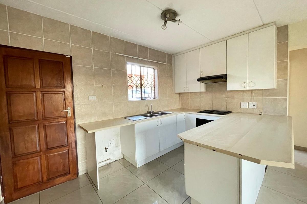 A functional kitchen featuring white built-in cabinetry, tiled splashbacks, a double sink, and a built-in hob with an extractor fan.