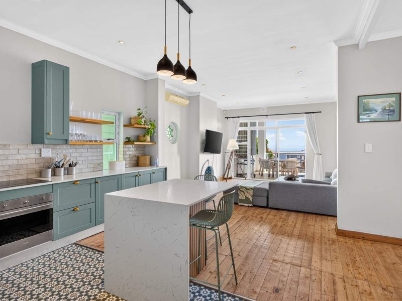 Modern open-plan living area featuring a stylish kitchen with stone island, built-in appliances, and seamless flow to a balcony with scenic views.