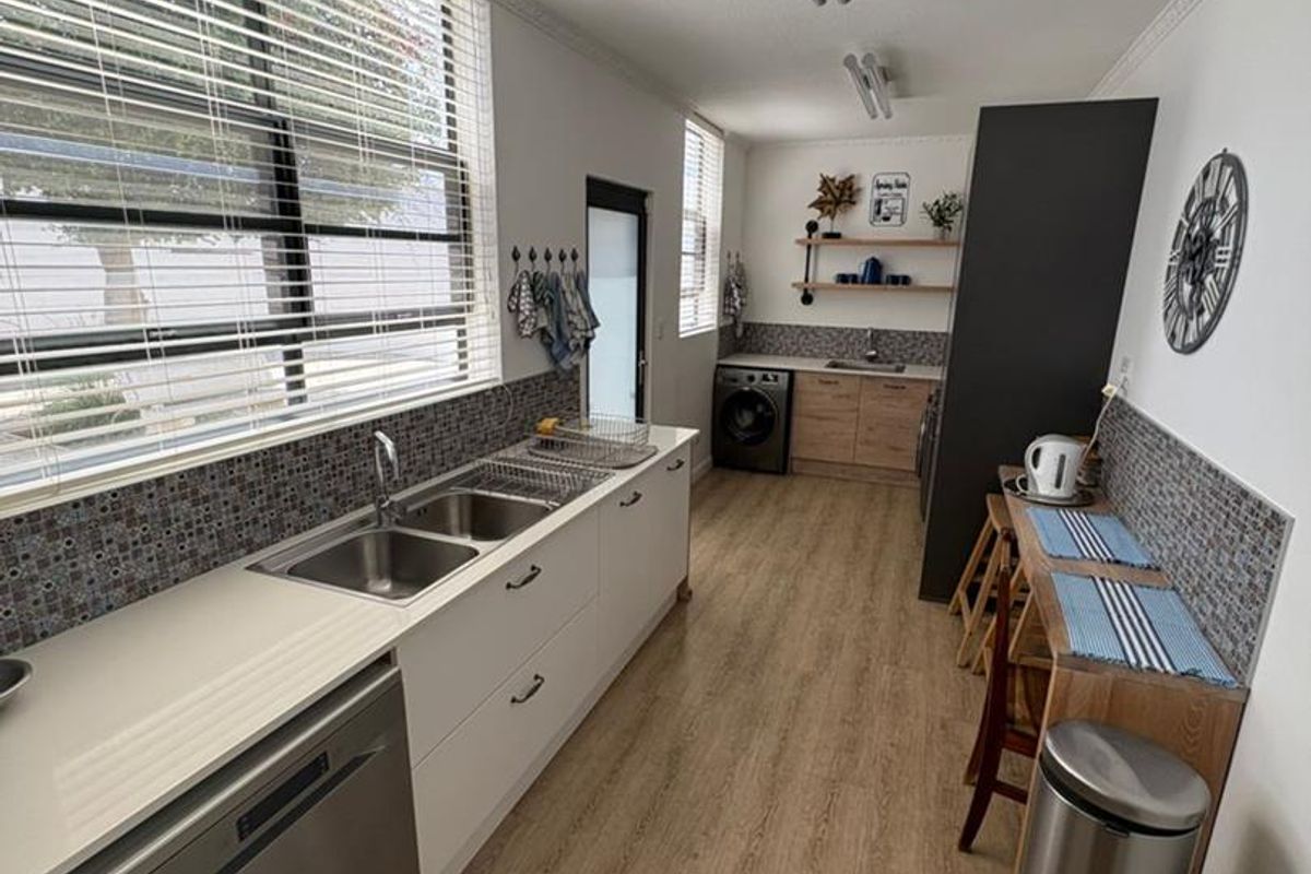 A functional galley-style kitchen and laundry area featuring modern cabinetry, integrated sink, mosaic tile backsplash, and wood-look flooring.