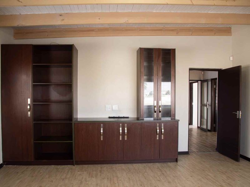 A spacious living area featuring built-in dark wood cabinetry, exposed timber ceiling beams, and modern laminate flooring, offering a clean and functional layout.