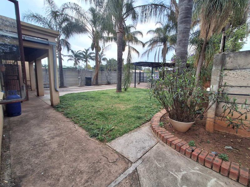 A rear garden area featuring a concrete patio, lawn, perimeter wall, and a covered carport structure.