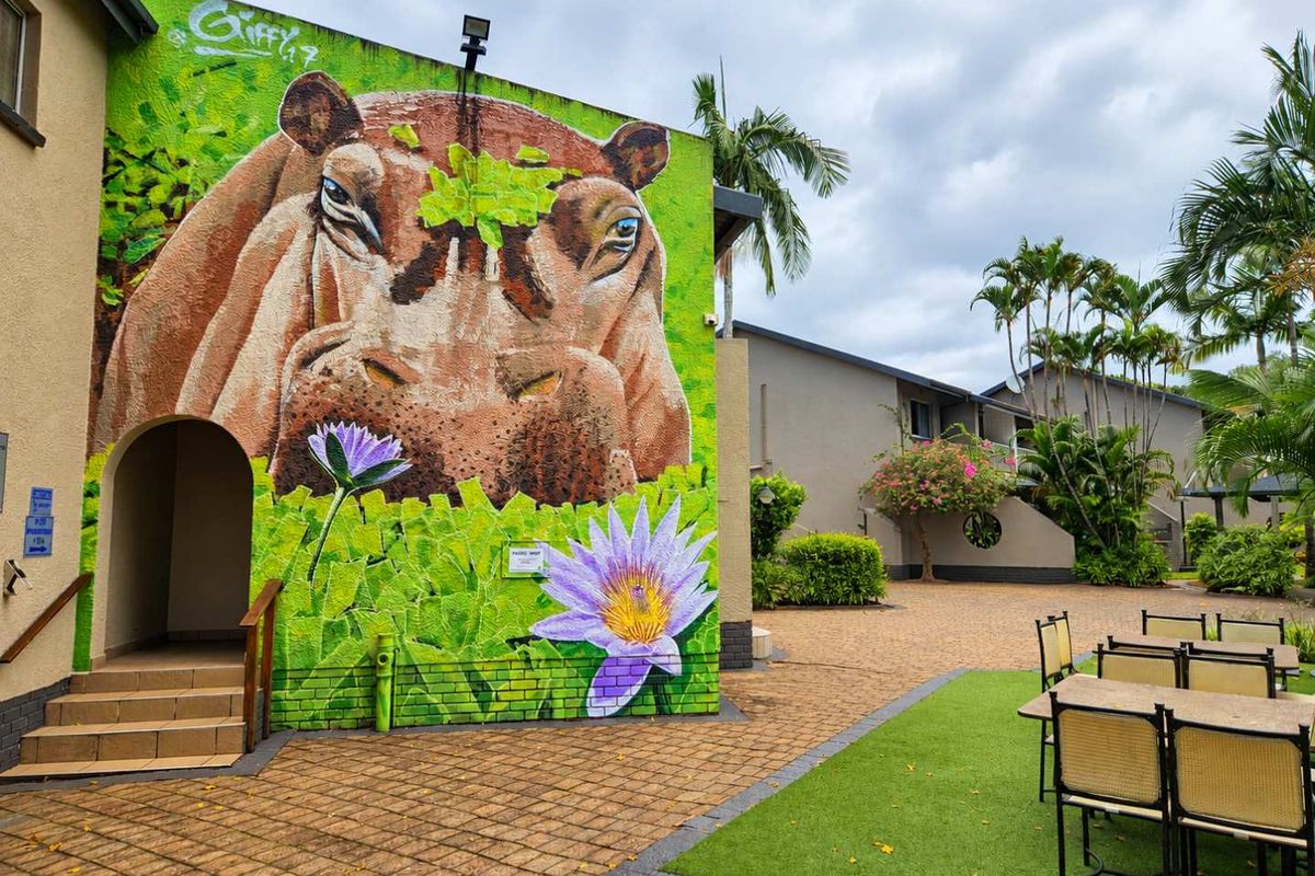 A well-maintained exterior courtyard area featuring a large decorative mural on the building facade, paved walkways, and an artificial grass seating area.