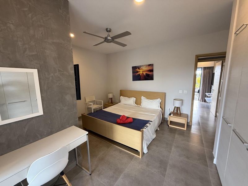 A well-maintained bedroom featuring large format floor tiles, a textured feature wall, a ceiling fan, and direct access to an adjoining bathroom.