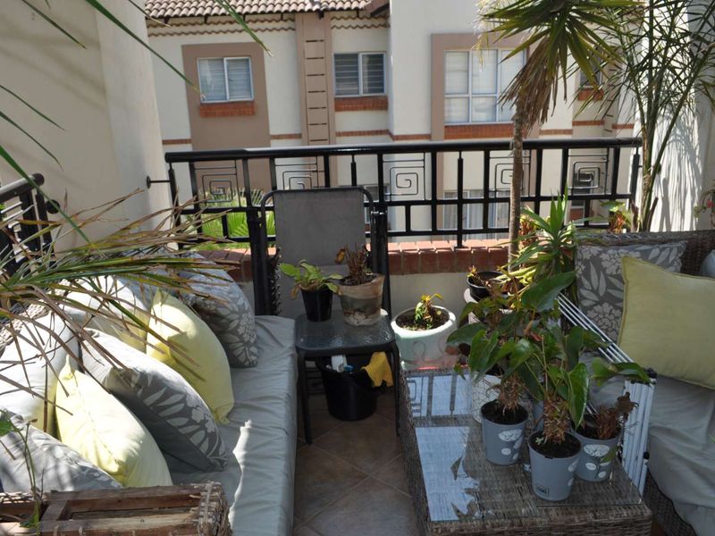 A covered balcony featuring tiled flooring and a decorative metal balustrade, overlooking the apartment complex courtyard.
