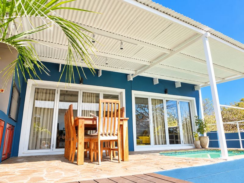 A covered outdoor patio featuring a corrugated metal roof, track lighting, and stone paving, providing direct access to the swimming pool area.