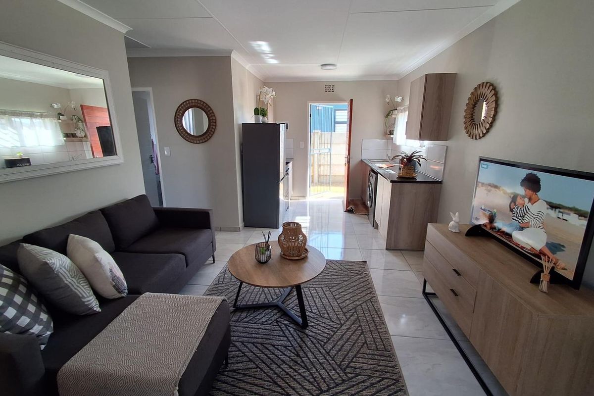 An open-plan living area featuring tiled flooring, a compact kitchen with built-in cabinetry, and direct access to an exterior space.
