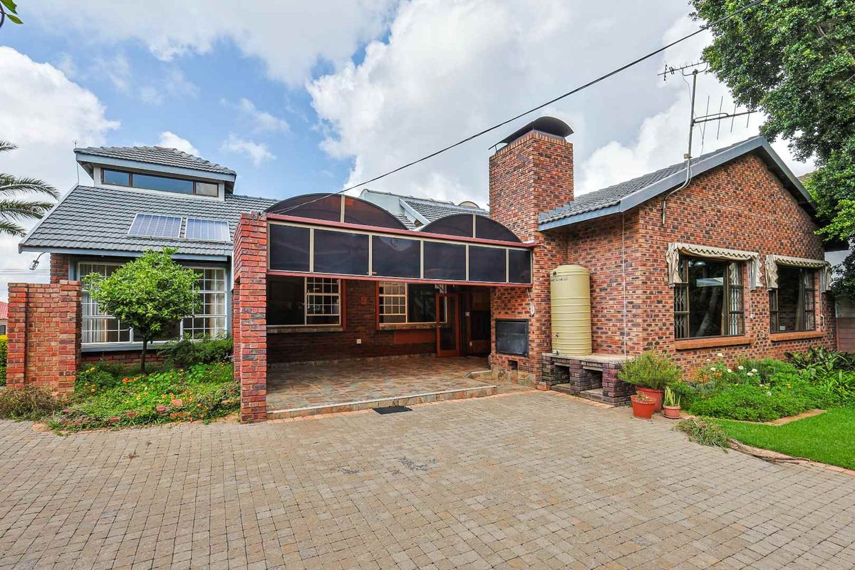 Rear exterior view of a brick house featuring a covered patio area, built-in braai, water storage tank, and solar panels on the roof.