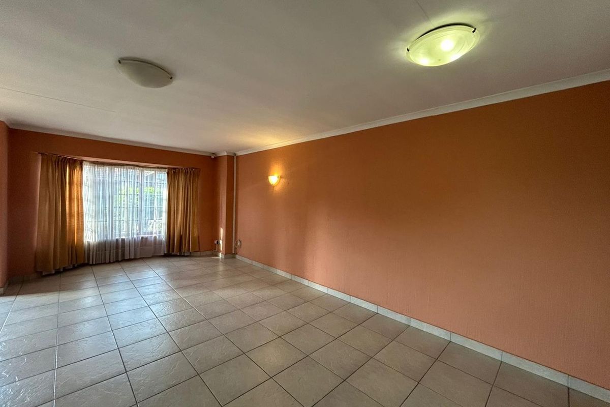 A spacious, empty living room featuring tiled flooring, warm-toned walls, and large windows with curtains, providing a blank canvas for personalization.