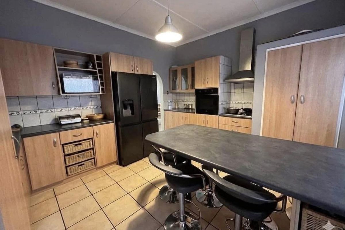 A functional kitchen featuring wood-finish cabinetry, dark countertops, a central island, and tiled flooring, providing a practical workspace for daily cooking and dining.