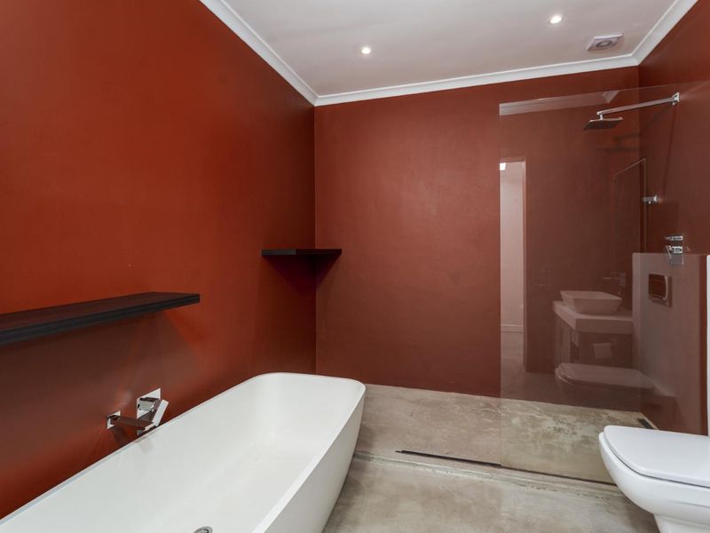 Modern bathroom featuring a freestanding bathtub, walk-in shower with glass screen, wall-mounted toilet, and polished concrete flooring with bold red accent walls.