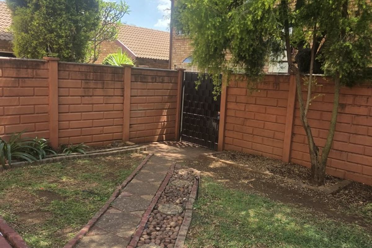 A private rear garden area featuring a brick boundary wall, metal access gate, and a paved pathway with decorative pebble edging.