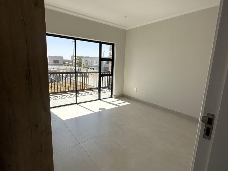 A bright, empty bedroom featuring modern tiled flooring, recessed lighting, and a large sliding glass door providing access to a private balcony.