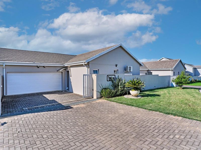 Front view of a well-maintained house featuring a paved driveway, automated garage, and secure boundary wall with landscaped garden area.